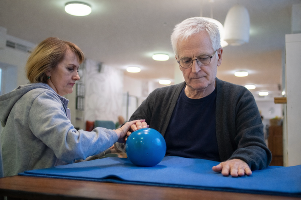 Пациент во время занятия с эрготерапевтом разрабатывает слабую руку с помощью мяча