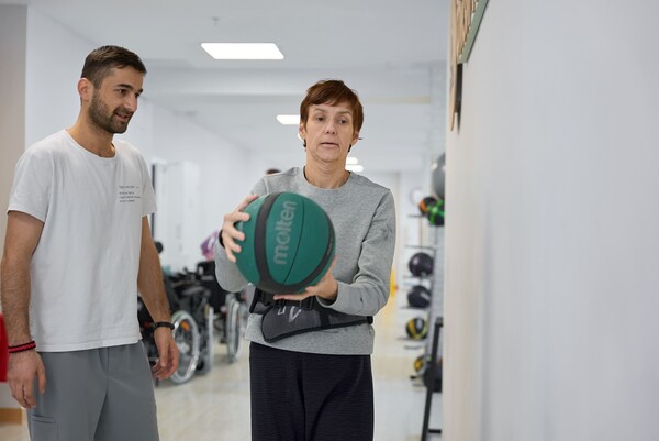 Пациентка во время реабилитации на занятии с физическим терапевтом. Для тренировки баланса держит в руках мяч