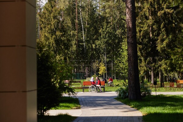 Пациент в коляске рядом с родственником во дворе клиники «Три сестры»