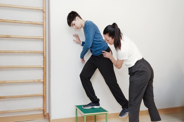 Молодой человек с ДЦП в зале физической терапии с терапевтом